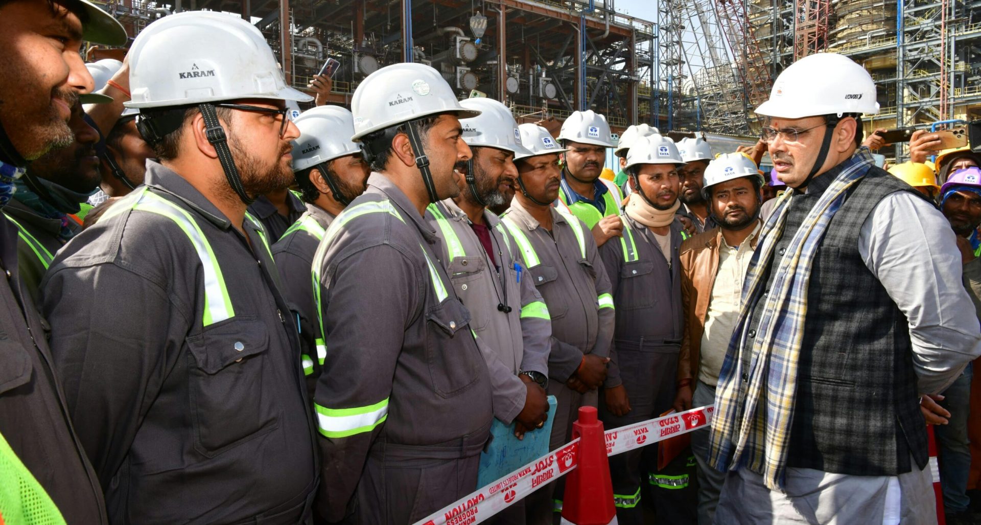 Construction workers in hard hats gathered on an industrial site for a briefing.